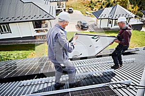 Technicians carrying photovoltaic solar module while installing solar panel system on roof of house