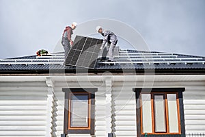 Technicians carrying photovoltaic solar module while installing solar panel system on roof of house