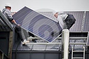 Technicians carrying photovoltaic solar module while installing solar panel system on roof of house