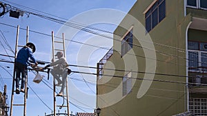 Technicians on wooden ladders are working to install telephone wires on electric pole