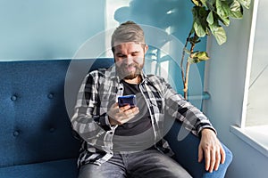 Technologies and leisure concept - Cheerful man sitting on the couch using his smartphone at home in the living room.