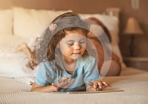 Technology for all ages. an adorable little girl at home lying on her bed playing with a tablet.