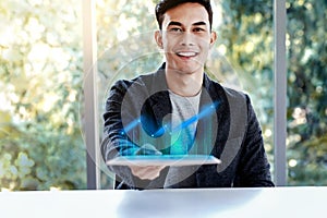 Technology in Business Concept. Happy Young Man Sitting at the Desk and presenting High Profit Graph in Digital Tablet