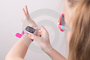 Technology for children: a girl wearing pink glasses uses a smartwatch.