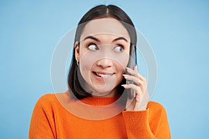 Technology concept. Close up of smiling asian woman talks on mobile phone, having conversation on cellphone, blue