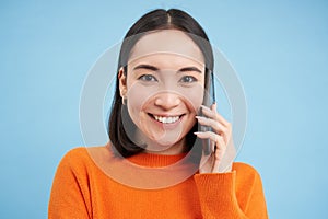 Technology concept. Close up of smiling asian woman talks on mobile phone, having conversation on cellphone, blue