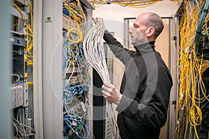 Technology Concept. A man works with communication cables in a data center. A technician stacks a wiring harness in a server room