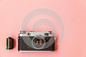 Vintage film photo camera lens and film roll on pink pastel trendy background