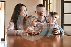 Technology has its place in a modern home. a young family of four using a digital tablet together at home.