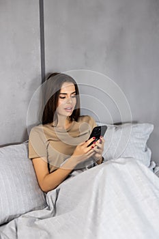 Technology, internet, communication and people concept. happy smiling young woman texting on smartphone in bed at home bedroom at