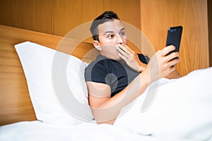 Technology, internet, communication and people concept - young man get a sms with surprise news in bed at home in morning