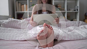 Technology, internet and people concept - happy young woman lying in bed with tablet pc computer at home bedroom