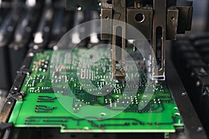 Technology and its basics. Macro closeup shot. Vivid green printed circuit board and moving part of SMD montage machine.