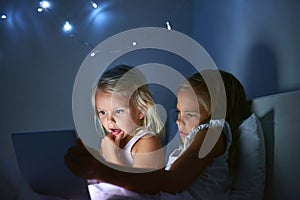 Technology keeps them entertained during the day and night. two little girls using a digital tablet before bedtime.