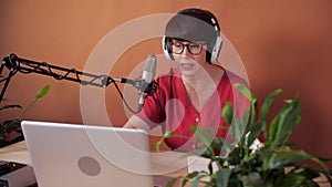 Technology and mass media concept. Middle-aged woman with microphone and laptop computer talking and recording podcast