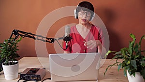 Technology and mass media concept. Middle-aged woman with microphone and laptop computer talking and recording podcast