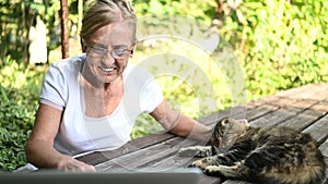 Technology, old age people concept - elderly happy senior woman with home cat working online with laptop computer outdoors