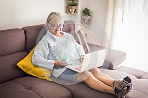 Technology, old age and people concept - happy senior woman in glasses with laptop computer and glass of the at home