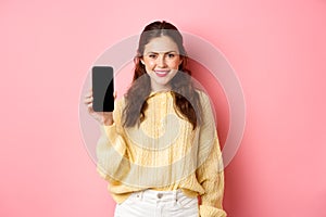 Technology and online shopping. Young smiling woman looking determined, advicing download app, showing smartphone app on