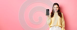 Technology and online shopping. Young smiling woman looking determined, advicing download app, showing smartphone app on