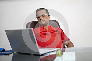 Technology, remote job and lifestyle concept - happy indian man in glasses with laptop computer working at office