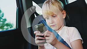 Technology on the road. The girl is 6 years old playing on a smartphone, she is riding a car seat