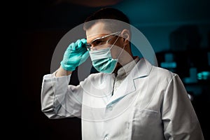 Technology, science, and people concept - male doctor or scientist in white coat and safety glasses, mask and gloves