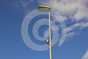 Technology view of light sensor on street lighting pole on blue sky with rare white clouds background.