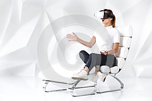 Technology, virtual reality, entertainment and people concept - happy young woman with virtual reality headset sits on a