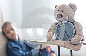 Teddy bear with alarm clock on a blurred background of the children`s room