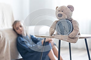 Teddy bear with alarm clock on a blurred background of the children`s room