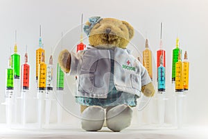 Teddy bear as a woman doctor with plastic medical syringes containing multicolor solutions and white background.`Medical concept`