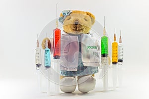 Teddy bear as a woman doctor with plastic medical syringes containing multicolor solutions and white background.`Medical concept`