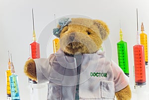 Teddy bear as a woman doctor with plastic medical syringes containing multicolor solutions and white background.`Medical concept`