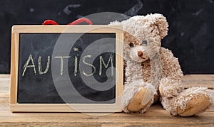Teddy bear and a blackboard. Autism text drawing on the blackboard