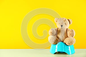 Teddy bear with blue potty on table against yellow background. Toilet training photo