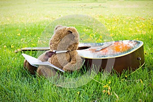 Teddy bear on classical guitar on field.