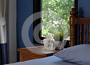 A teddy bear,coffee cup and white alarm on wood table in blue bedroom