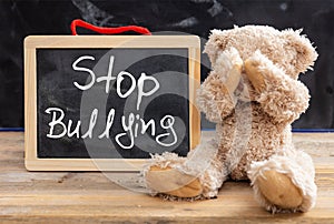 Teddy bear covering eyes and stop bullying text on a blackboard