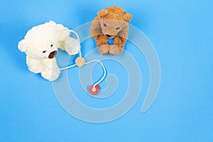 Teddy bear doctor with stethoscope and teddy bear patient on light blue background with wooden toy medicine tools