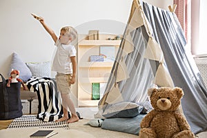 Teddy bear on the floor of stylish single child playroom with tent and toys, real photo