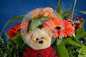 Teddy bear in front of a flower bouquet Orange flowers