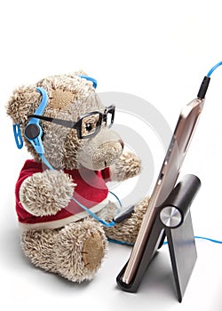 Teddy bear with glasses and headphones sitting looking at the mobile phone