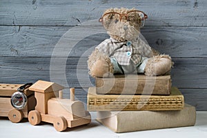 Teddy bear in glasses on the old books and wooden toy train