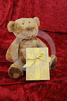Teddy bear with golden gift box on red