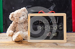 Teddy bear hiding behind a blackboard. Special needs text drawing on the blackboard