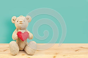 Teddy bear holding heart on wood table on blue background