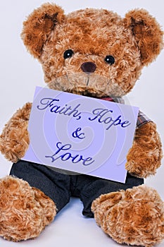 Teddy bear holding a purple sign that says Faith, Hope and Love