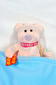 Teddy bear laying in bed with thermometer