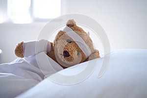 Teddy bear lying sick in bed With a headband and a cloth covered